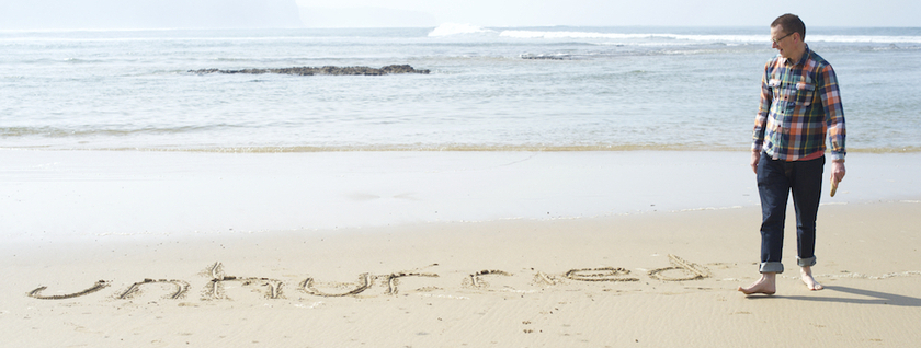 Man walking on a beach, with the word unhurried etched in the sand